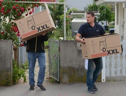 <p>
	Beamte tragen in Fellbach Kisten aus einem durchsuchten Haus.</p>
