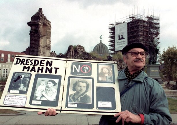 <p>
	Ein Mann hält 1992 vor der Ruine der Frauenkirche in Dresden ein Mahnplakat mit Fotos. Während die britische Königin Elizabeth II. an der Frauenkirche, die 1945 bei einem alliierten Luftangriff zerstört wurde, vorbeifährt, macht er auf das Schicksal seiner Familie aufmerksam, die bei dem Luftangriff auf Dresden starb.</p>
