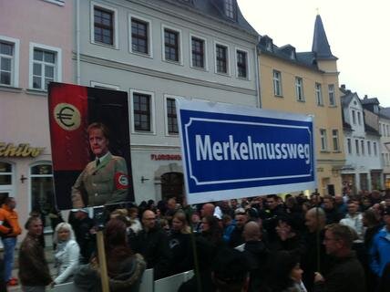 <p>
	... wurde unter anderem ein Plakat mit Angela Merkel in Nazi-Uniform und durch Eurozeichen verfremdeter Hakenkreuz-Armbinde gezeigt. Teilnehmer riefen „Merkel muss weg“, „Wir sind das Volk“ und „Abschieben!“.</p>
