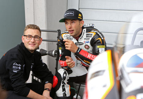 <p>Teamchef Florian Prüstel vom Team Peugeot MC Saxoprint unterhält sich in der Boxengasse mit seinem Daher Jakob Kornfeil.</p>
