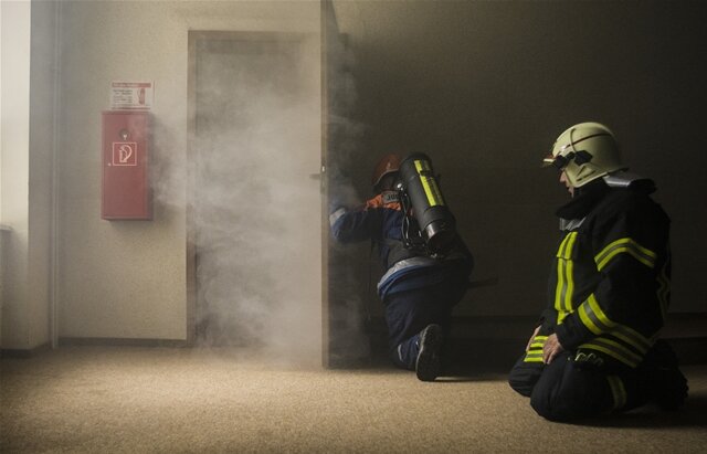 <p>Bei der Öffnung einer Tür zum Brandraum muss der Feuerwehrmann auf seinen Eigenschutz achten. Max Müller (l.) trägt eine Atemschutztechnikatrappe.&nbsp;Hilfestellungen bekommt er von Marek Göthel (r.).</p>
