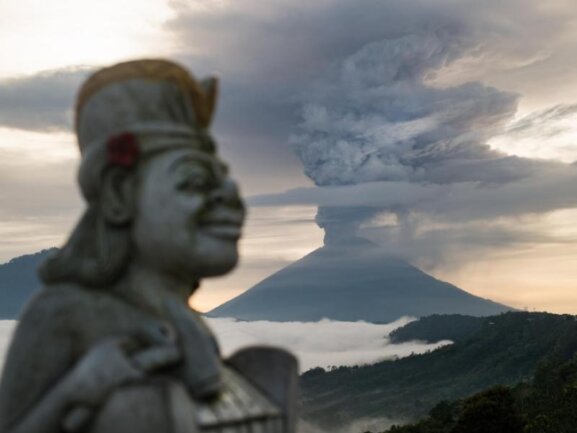 <p>Entrücktes Lächeln:&nbsp;Eine Statue ist neben der riesigen Rauchsäule zu sehen, die über dem balinesischen Vulkan Mount Agung aufsteigt.</p>
