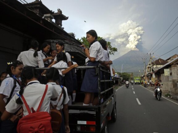 <p>Auf dem Weg zur Schule:&nbsp;Balinesische Jugendliche klettern auf einen Pick-up, während der Mount Agung im Hintergrund Rauch und Asche spuckt.</p>
