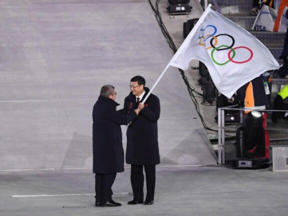 <b>Übergabe</b><br/>IOC-Präsident Thomas Bach (l) übergibt die olympische Flagge an Pekings Bürgermeister Chen Jining. Foto: Hendrik Schmidt<br/>25.02.2018 (dpa)