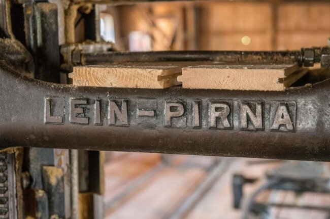 <p>Diese beiden Bretter sind in ein Sägegatter eingespannt. Der Hersteller des Gatters war die Firma „Gebrüder Lein“ aus Pirna. Das Unternehmen wurde 1885 gegründet und stellte Maschinen für Holz- und Papierfabriken sowie Steinsägen her. Nach dem Zweiten Weltkrieg wurde die Firma Lein enteignet, die Fertigungsanlagen demontiert.</p>
