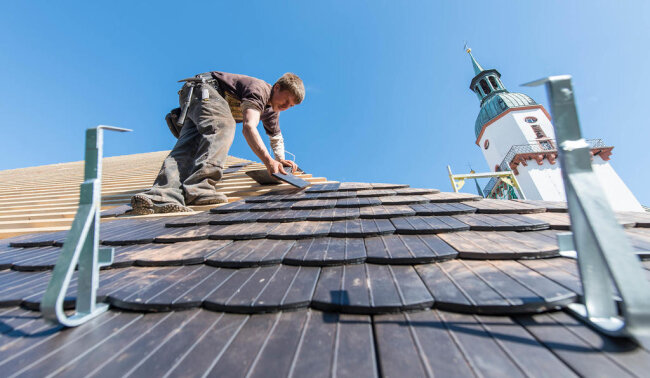 <p>Handarbeit in luftiger Höhe auf der Baustelle der Stadtbibliothek: Mitarbeiter einer Dachbaufirma decken im März 2019 das Dach mit Biberschwanzziegeln.</p>
