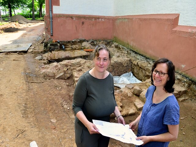 <p>Rebecca Wegener (l.) und Daniela Frehse vor den Resten eines älteren Fundaments an der Außenwand.</p>
