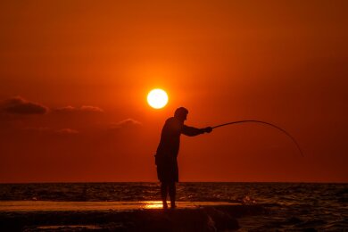 Alltag im Libanon: Ein Fischer wirft seine Angel von einem felsigen Gebiet entlang der Küste von Beirut aus, während die Sonne über dem Mittelmeer untergeht.