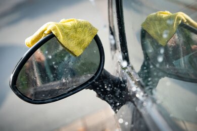 Illustration - Ein Lappen liegt während einer Autowäsche auf dem Seitenspiegel eines Fahrzeugs.