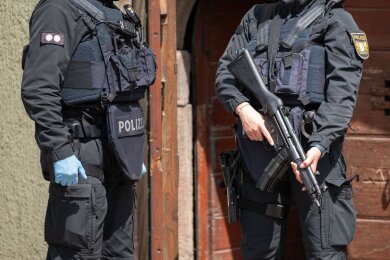 Eine Polizistin (r) steht mit einer Maschinenpistole vor einer Tür in Althengstett.