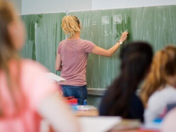            Eine junge Lehrerin schreibt im Unterricht an eine Schultafel.