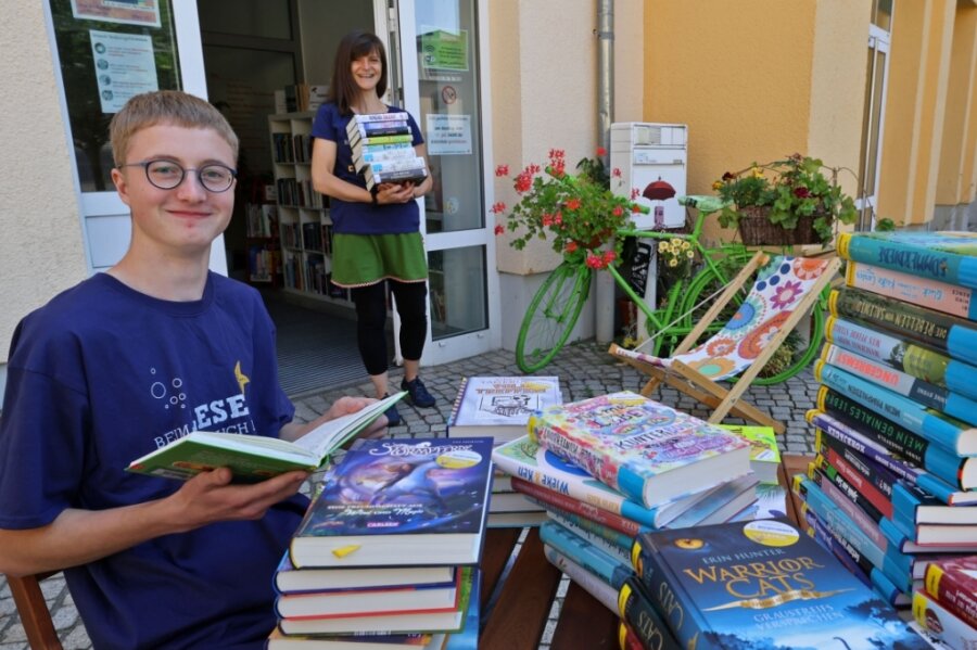 Stapelweise neue Jugendbücher gibt's beim Buchsommer in der Stadtbibliothek Lichtenstein. Timon Grießbach (links) sichtet im Büchergarten die Lektüre. Im Hintergrund Mitarbeiterin Peggy Hartmann. 