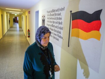 17. Was sind sichere Herkunftsländer? - Eine Frau mit Kopftuch in der Erstaufnahmeeinrichtung für Flüchtlinge in Stern-Bucholz bei Schwerin (Mecklenburg-Vorpommern). An der Wand sind neben der Deutschlandfahne ist der Text der deutschen Nationalhymne zu sehen.