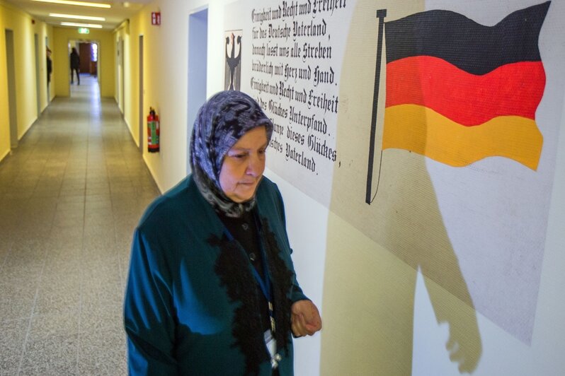 Eine Frau mit Kopftuch in der Erstaufnahmeeinrichtung für Flüchtlinge in Stern-Bucholz bei Schwerin (Mecklenburg-Vorpommern). An der Wand sind neben der Deutschlandfahne ist der Text der deutschen Nationalhymne zu sehen.