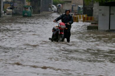Ein Pakistaner watet nach starken Regenfällen mit seinem Motorrad durch eine überschwemmte Straße in Peschawar.