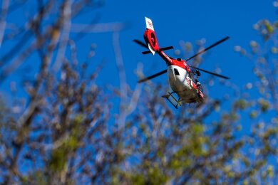 Ein Helikopter der DRF Luftrettung schwebt am Himmel über einem Waldstück.