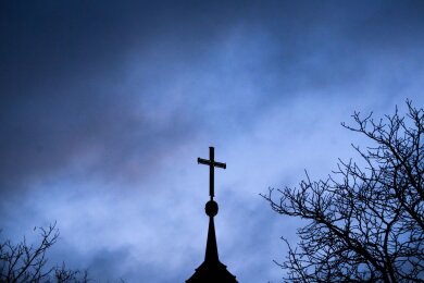 Dunkle Wolken ziehen über das Kreuz auf einer Kirche hinweg.