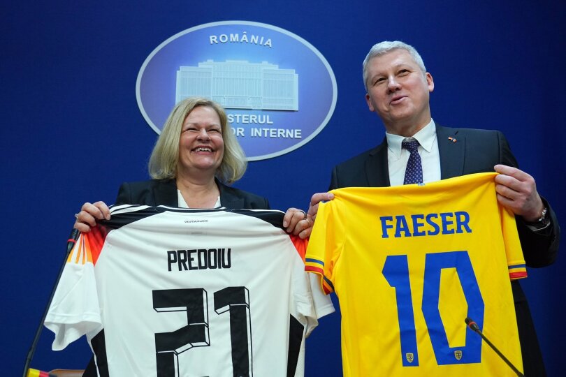 Nancy Faeser (SPD), Bundesministerin des Innern und Heimat, und Marian Catalin Predoiu, Vizepremierminister und Innenminister von Rumänien, halten nach einer gemeinsamen Pressekonferenz die T-Shirts der jeweiligen Fussball-Nationalmannschaft in den Händen.