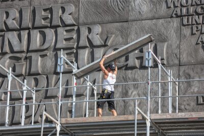 Gerüstbauer sind hinterm Nischel am historischen Schriftzug an der Fassade des langen Behördenriegels zu Gange.
