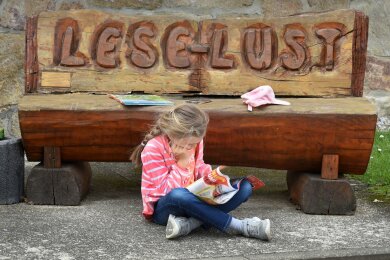 Ein Kind sitzt lesend vor der "Lese-Lust"-Bank an der Schule in Mügeln. Das Kultusministerium verlängert das Projekt "Lesescouts" der Stiftung Lesen um zwei weitere Jahre (2024 und 2025) und unterstützt es finanziell mit 50.000 Euro.