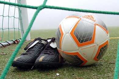 Fußballschuhe und ein Ball liegen hinter einem Tornetz.
