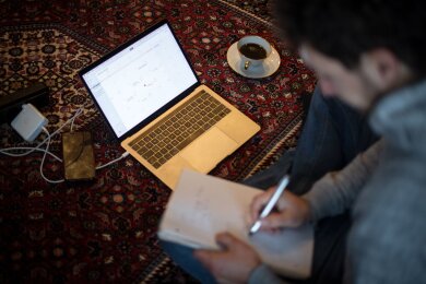 Ein Mann sitzt im Homeoffice mit Laptop auf dem Teppich und arbeitet.