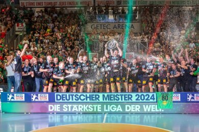 Christian O Sullivan (M) hebt die Meisterschale in die Höhe und jubelt mit Teamkollegen des SC Magdeburg hinter Schriftzug: Deutscher Meister 2024.