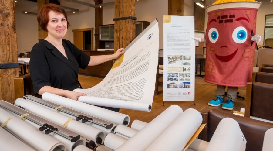 Susann Hofmann, Amtsleiterin für Kultur und Tourismus der Stadt Marienberg, zeigt gemeinsam mit Fest-Maskottchen Uli zwei der insgesamt 78 zur Marienberger Handelsgeschichte entstandenen Banner. 
