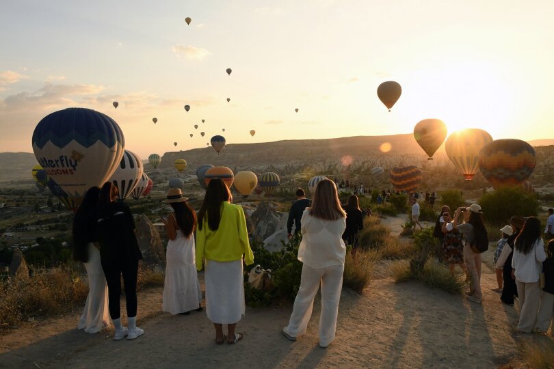 Zahlreiche Schaulustige bestaunen wie im türkischen Kappadokien Heißluftballons über Gesteinsformation Kappadokien fliegen.