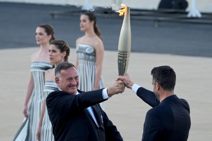 Der französische Präsident Tony Estanguet erhält die olympische Flamme von Spyros Capralos, dem Vorsitzenden des griechischen Olympischen Komitees, im Panathenäischen Stadion in Athen, wo 1896 die ersten modernen Spiele stattfanden.