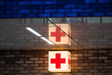 Ein Leuchtkasten mit einem roten Kreuz hängt vor der Notaufnahme eines Krankenhauses.