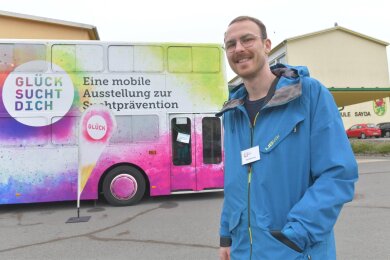 Nils Biedermann koordiniert die Aktion „Glück sucht dich“ in Sachsen. Im Hintergrund: Der Präventionsbus mit der mobilen Ausstellung zur Suchtprävention.