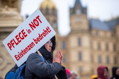 Bei einer Protestaktion vor dem Schweriner Landtag hält eine Teilnehmerin ein Schild mit der Aufschrift "Pflege in Not - Existenzen bedroht!".