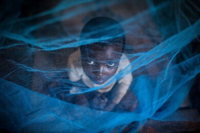 Ein Flüchtlingskind aus Burundi sitzt in Gashora, Ruanda, unter einem Moskitonetz: Der Malaria-Erreger wird durch Anopheles-Stechmücken übertragen.
