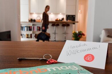 Ein Schlüssel mit einem Airbnb-Anhäger, ein Magazin und eine Herzlich-Willkommen-Karte liegen in der Wohnung eines Airbnb-Gastgebers. Das bei Reisenden beliebte Modell zwingt Großstädte mit knappem Wohnraum zur Verhängung von Bußgeldern.