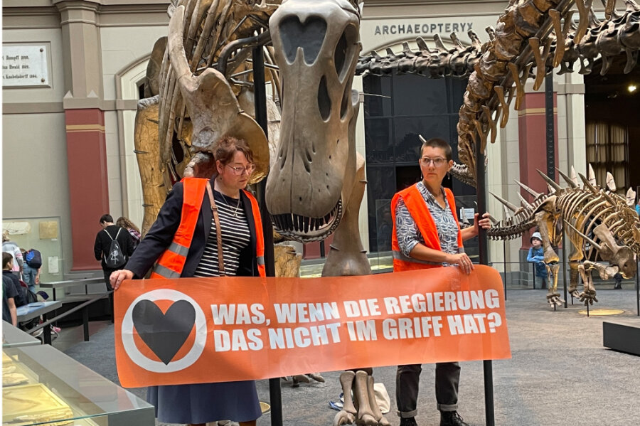 Aktivistinnen kleben sich an Dinosaurier im Berliner Naturkundemuseum fest - Zwei Klimaaktivistinnen mit einem Banner "Was, wenn die Regierung das nicht im Griff hat?" haben sich im Berliner Museum für Naturkunde an den Haltestangen eines Dinosauriers festgeklebt. 