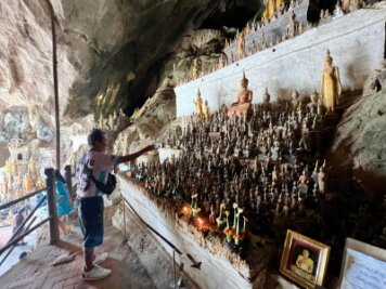 Am Mekong: Heilige Höhlen mit 6000 Buddha-Statuen - Ein Mann besprenkelt Buddha-Statuen in den Pak Ou Caves als Zeichen des tiefen Respekts mit Wasser.