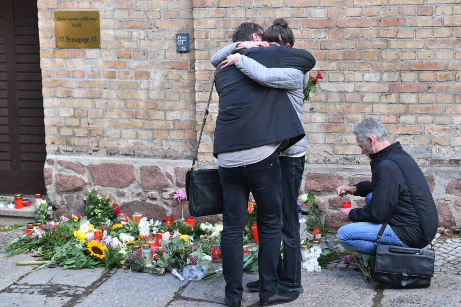 Menschen trauern vor Kerzen und Blumen an der Synagoge. 