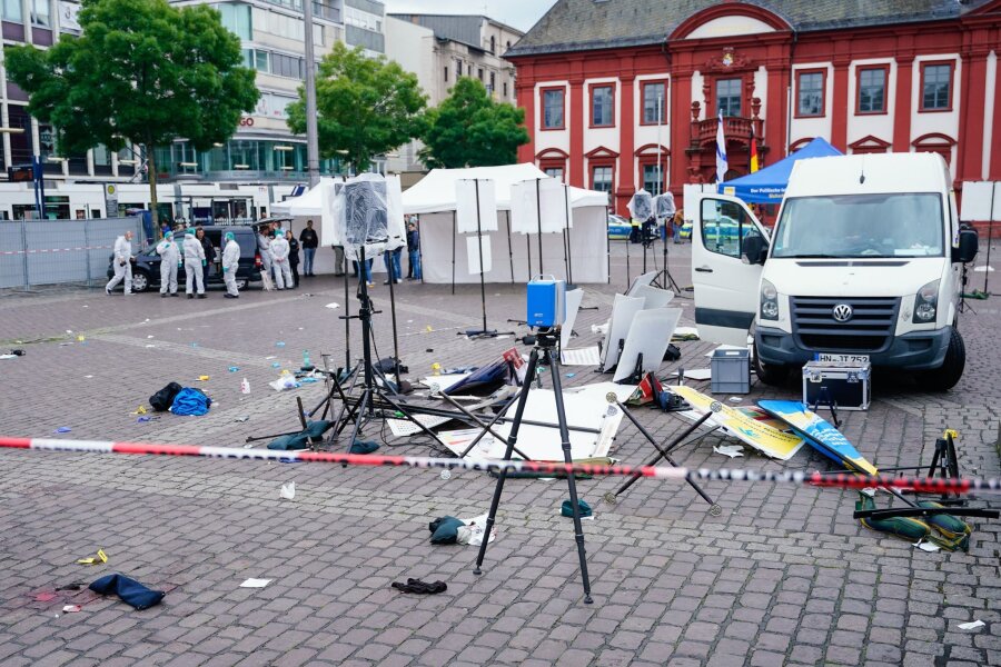 Angriff in Mannheim löst neue Debatte über Abschiebungen aus - Mitarbeiter der Spurensicherung stehen auf dem Marktplatz hinter einem zertrümmerten Stand.