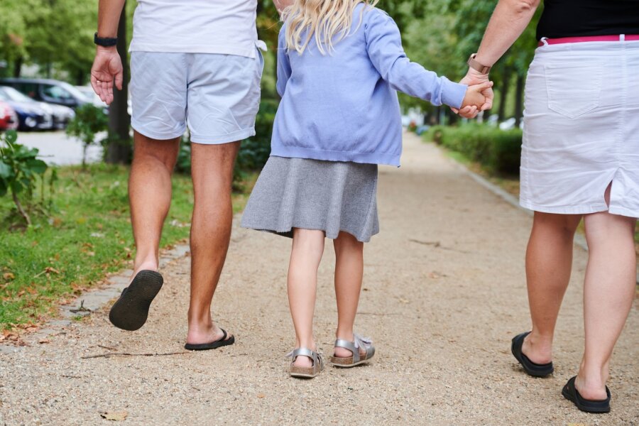 Anzahl der Familien mit minderjährigen Kindern gestiegen - Ein Vater und eine Mutter halten die Hände ihrer Tochter, während sie auf einem Gehweg gehen.