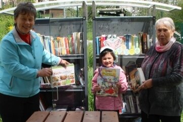 Kerstin Franke (l.) und Tamara Eidenschink gehören zu den Initiatoren der "Schmökerbox" an der Wanderhütte in Dänkritz. Die fünfjährige Lena hält in der ausgedienten Kühlzelle Ausschau nach Kinderbüchern.