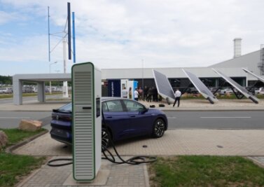 Ausgedienten E-Auto-Batterien wird zweites Leben eingehaucht - Der Schnellladepark im VW-Werk Mosel nebst Solar- und Windkraftanlagen. Im Vordergrund eine von vier Ladesäulen. Hinter dem Fahrzeug ist auf der anderen Straßenseite der Power Storage Container zu sehen. 