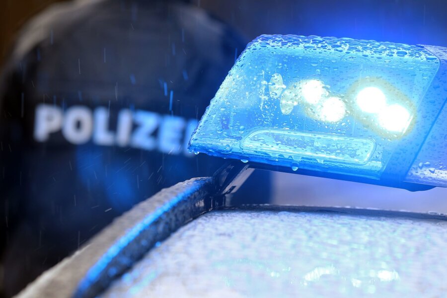 Auto fährt in Dresden Seniorin an: Tot - Ein Polizist steht im Regen vor einem Streifenwagen dessen Blaulicht aktiviert ist.
