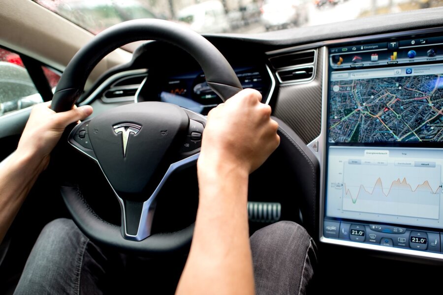 Autonomes Fahren: Klage gegen Tesla nimmt erste Hürde - Ein Mann sitzt in einem Tesla Model S am Lenkrad: Elon Musk sagt, er sei mit seinen Versprechen zu selbstfahrenden Autos oft zu optimistisch gewesen.