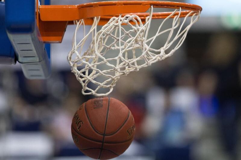            Ein Basketball fällt durch das Netz vom Basketballkorb.