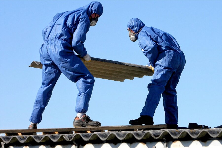 Bau-Gewerkschaft warnt vor „Asbest-Welle“ im Vogtland - Chef eines Plauener Großvermieters kontert: „Keine Panik“ - So sieht es aus, wenn Asbest-Altlasten fachgerecht beseitigt und entsorgt werden. Arbeiter in Schutzanzügen und mit Luftfiltern über Mund und Nase entfernen Asbestplatten vom Dach eines alten Gebäudes.
