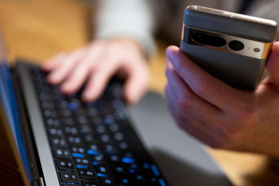 Betrugsmasche: Mails von angeblichen Auftragsmördern - Ein Mann sitzt am Laptop und hält ein Smartphone mit in der Hand.