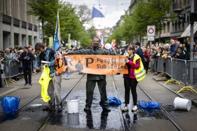 Bilder des Tages vom 15.04.2024 - Aktivisten protestieren während des traditionellen Umzugs der Zünfte beim Sechseläuten in Zürich gegen Subventionen für fossile Brennstoffe. Um ihre Botschaft zu verdeutlichen, begießen sie sich mit einer schwarzen Flüssigkeit.