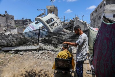 Bilder des Tages vom 25.05.2024 - Ein Stückchen Normalität: Ein Friseur arbeitet neben einer zerstörten Moschee nach einem israelischen Luftangriff auf die Stadt Deir al-Balah im Gaza-Streifen.
