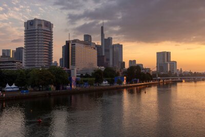 Bilder des Tages vom 28.06.2024 - Sonnenaufgang hinter der Frankfurter  Skyline - im Vordergrund das Ufer des Mains.